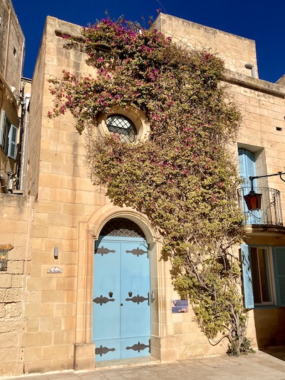 Blue door with purple flowers growing up the exterior in Mdina Malta