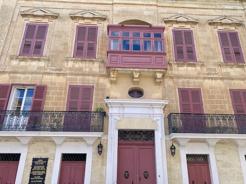 Building with pink shutters and wooden balcony in Pjazza San Pawl in Malta