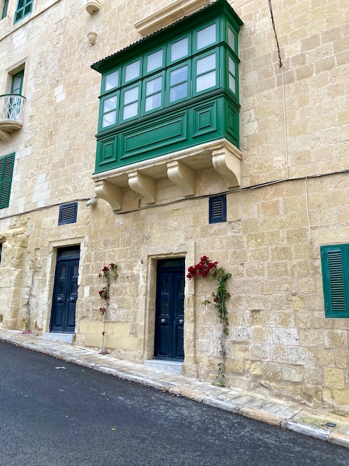 Front of traditional stone house with a brightly painted enclosed wooden balcony